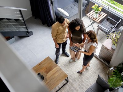 High angle view of a couple discussing details of a house with their real estate agent while looking at a brochure using a digital tablet