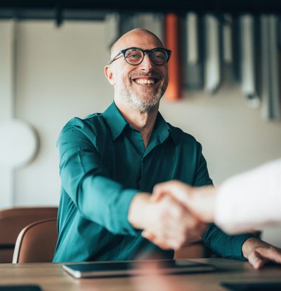 Two professionals shake hands over a signed contract, representing the successful conclusion of a business deal. This image embodies the spirit of collaboration and trust in a corporate environment. Business people shaking hands in the office. Portrait of cheerful manager handshake with new employee. Corporate business team on meeting in modern office. Company owner on a meeting with employee