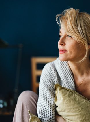 Close up shot of a beautiful blonde woman without makeup sitting on her bed in the morning. She is looking away.