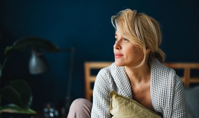 Close up shot of a beautiful blonde woman without makeup sitting on her bed in the morning. She is looking away.