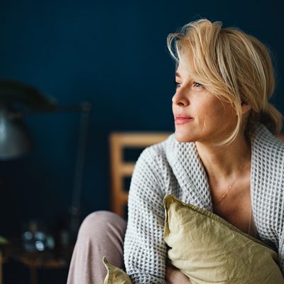 Close up shot of a beautiful blonde woman without makeup sitting on her bed in the morning. She is looking away.