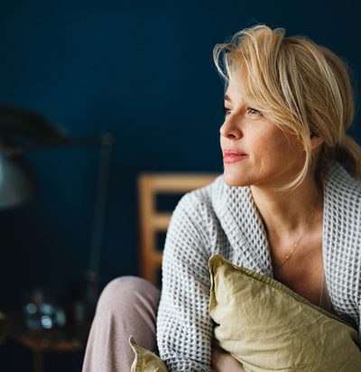 Close up shot of a beautiful blonde woman without makeup sitting on her bed in the morning. She is looking away.