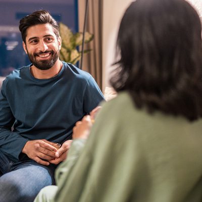 A cheerful young Arabic couple enjoys quality time together in a modern home, chatting comfortably on a beige sofa, highlighted by soft indoor lighting and contemporary decor.