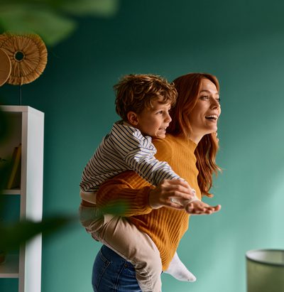 Happy mother giving her young son a joyful piggyback ride, laughing and having fun together in a domestic setting, celebrating family love and playful moments