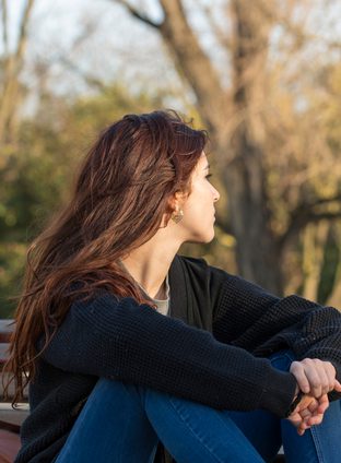Pensive young woman in the park looking away.