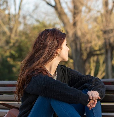 Pensive young woman in the park looking away.