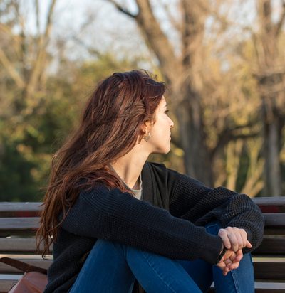 Pensive young woman in the park looking away.