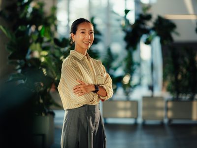 Portrait of a confident young asian businesswoman smiling with arms crossed in a modern office with plants