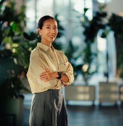 Portrait of a confident young asian businesswoman smiling with arms crossed in a modern office with plants