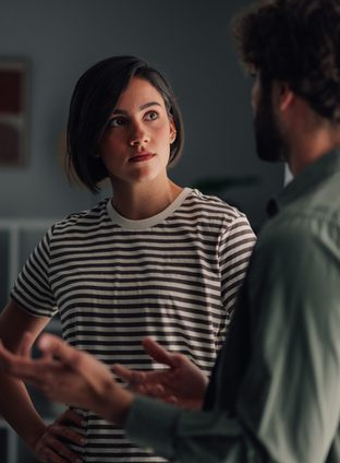 Young couple having serious discussion indoors. Woman listening intently to man talking, communicating relationship issues