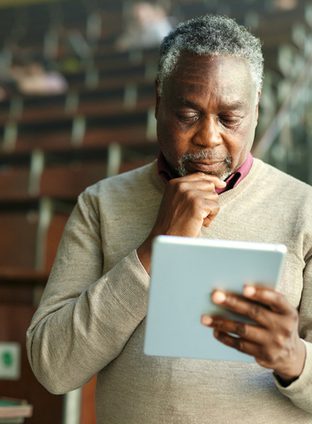 African American male teacher brainstorming while working on digital tablet during a class at lecture hall.