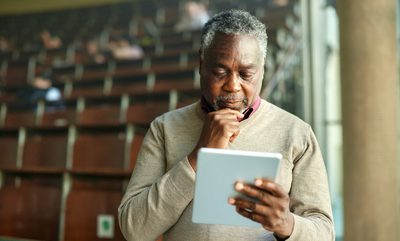 African American male teacher brainstorming while working on digital tablet during a class at lecture hall.