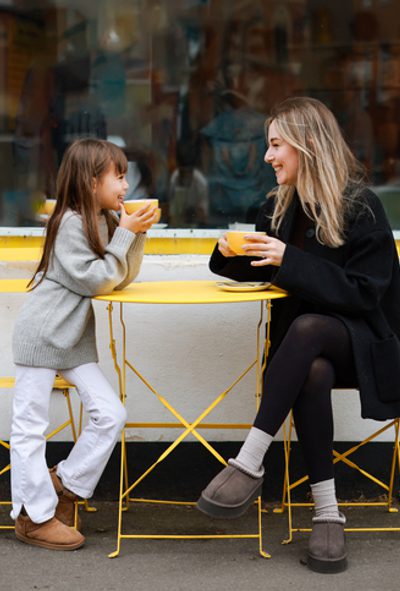 Young kid girl smiling. She sitting in cozy cafe with light interior and spending time with happy mum