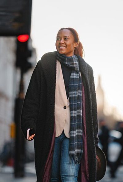 Young woman with phone and hat enjoys a walk in central London. Big Ben visible in the background, city street scene, modern fashion, cheerful atmosphere.