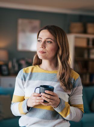 Mature woman looks out the window and drinks coffee.