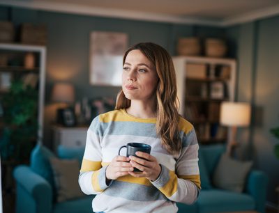 Mature woman looks out the window and drinks coffee.